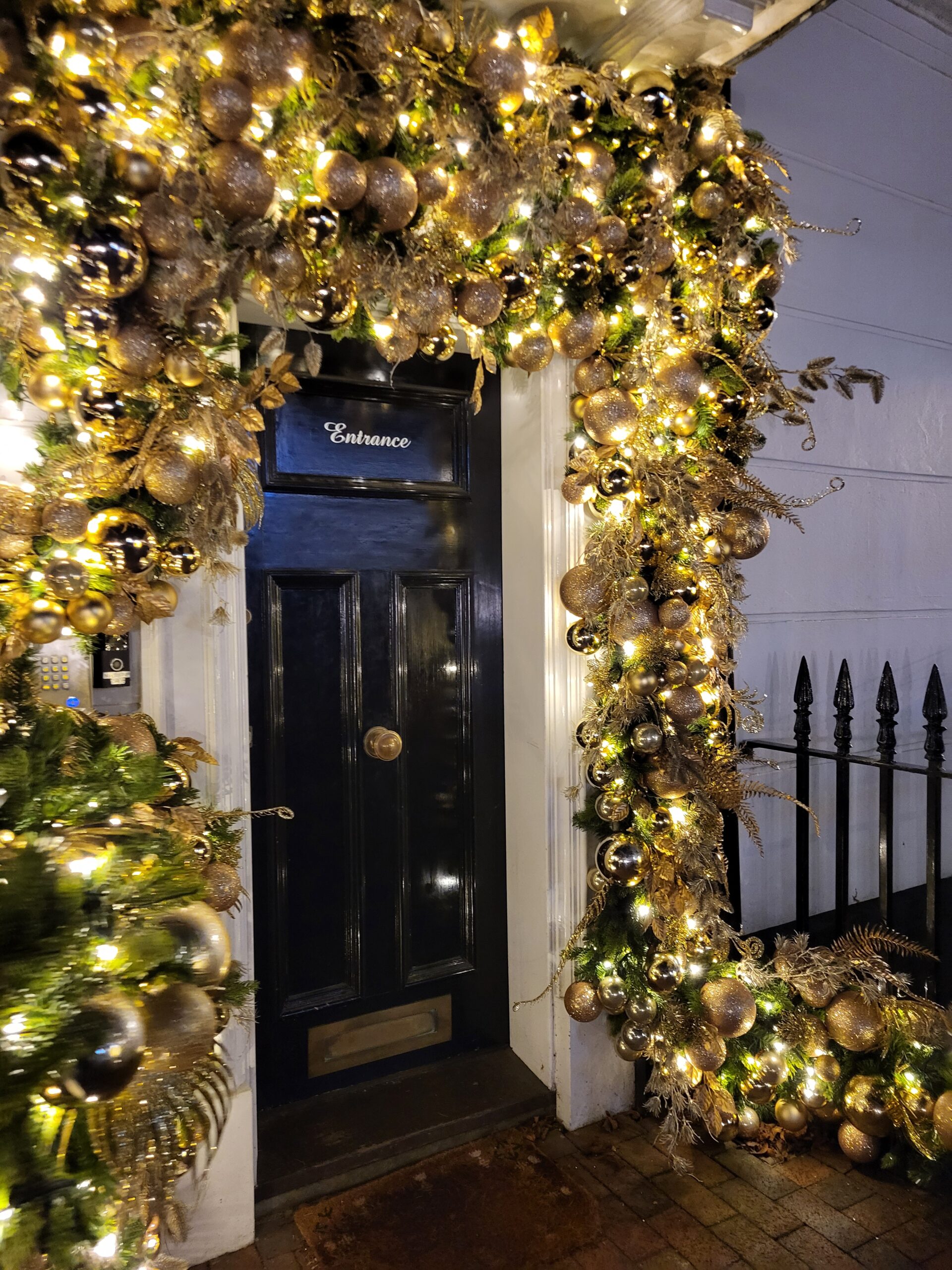 Gold and green decorative doorscape featuring Christmas baubles and florals.